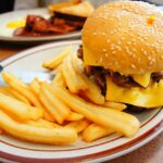 Piatto con alimenti da evitare per colesterolo alto: cibi fritti, formaggi grassi e salumi.